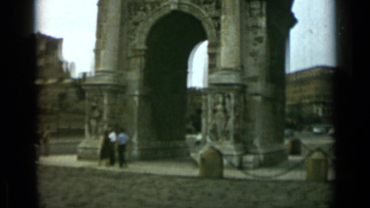 Closer view of the Arch of Constantine with pedestrians near the stone base and buildings behind.