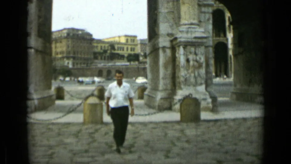 Closer 1962 Rome frame of the man approaching the camera through the stone arches, with carved surfaces and cobblestone texture prominent.