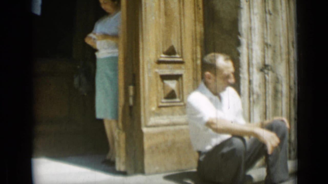 Man sitting on stone steps while a woman stands partly visible in the doorway behind him.