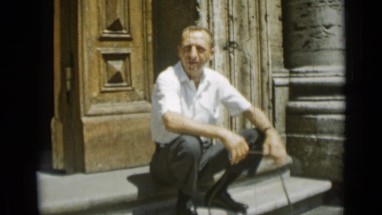 In Rome, Italy, a man sits on stone steps outside a classical building in 1962 home-movie footage.