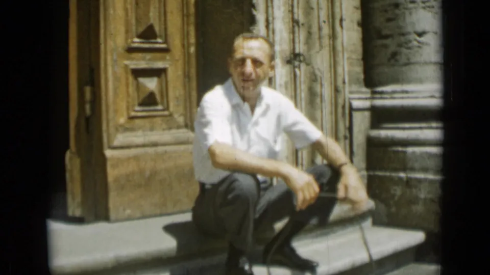 In Rome, Italy, a man sits on stone steps outside a classical building in 1962 home-movie footage.