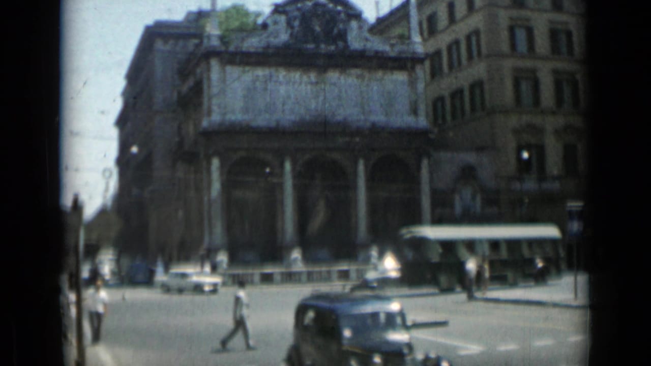 A Rome street intersection in 1962 shows cars, pedestrians, a bus, and an ornate columned building.