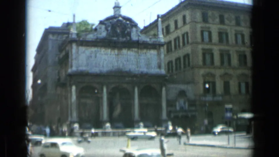 A 1962 Rome intersection shows mid-century cars, pedestrians, and an ornate building in soft 8mm color.