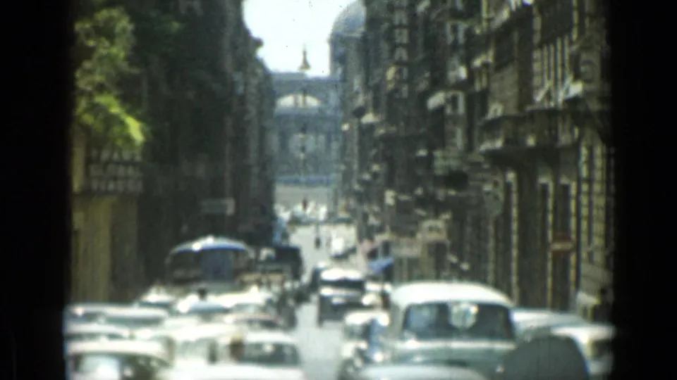 A Rome street scene shows dense mid-century car traffic between tall buildings, filmed in soft 8mm focus from street level.