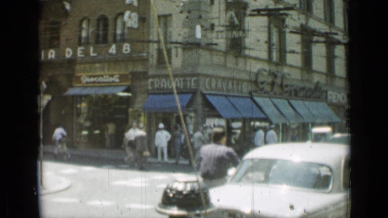 Rome street corner with pedestrians, classic cars, storefront awnings, and stone buildings.