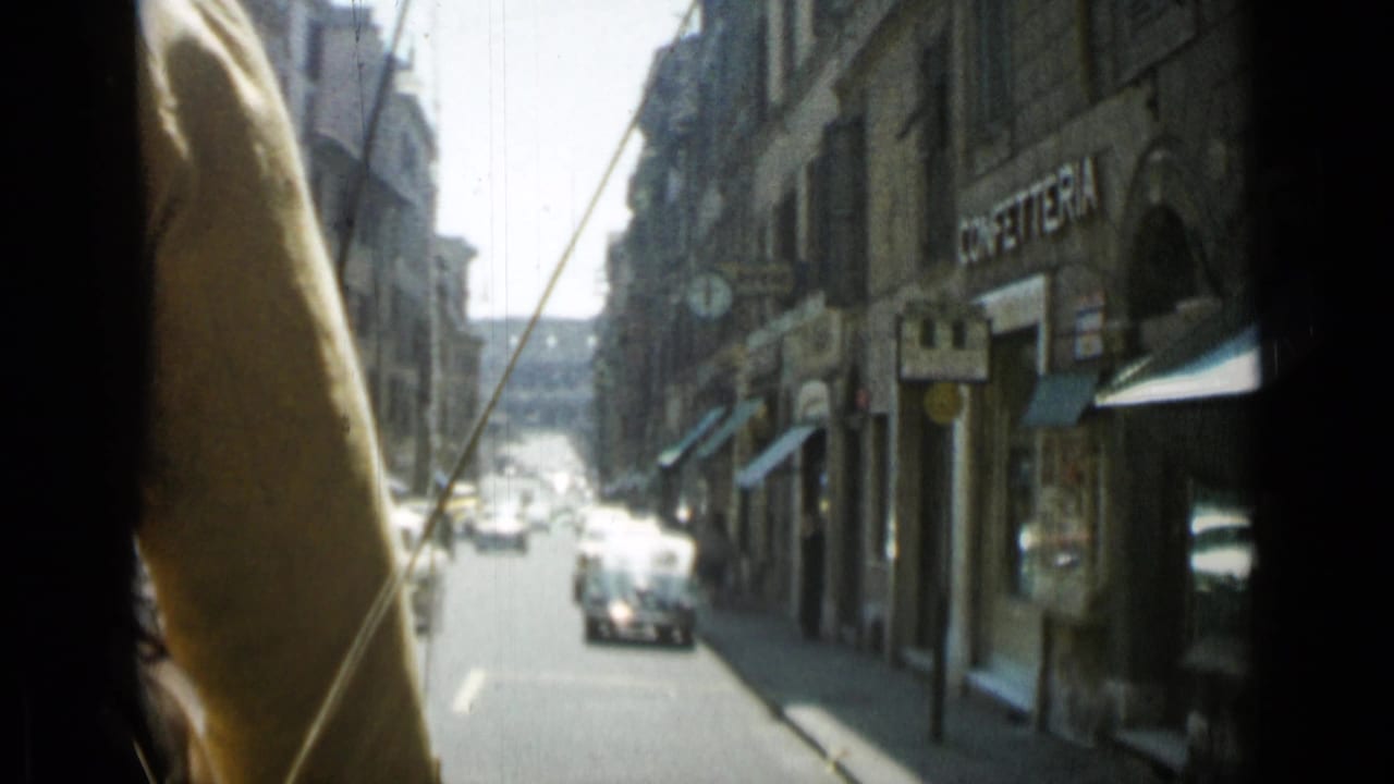 Narrow city street viewed past a dark window edge with cars and storefronts.