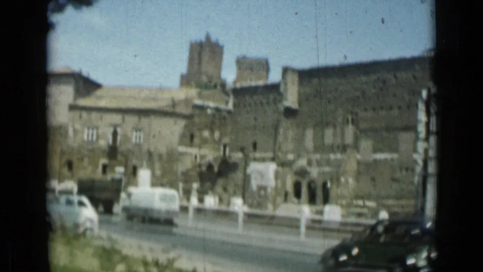 Rome street scene with moving and parked vehicles in front of large historic-looking stone buildings.