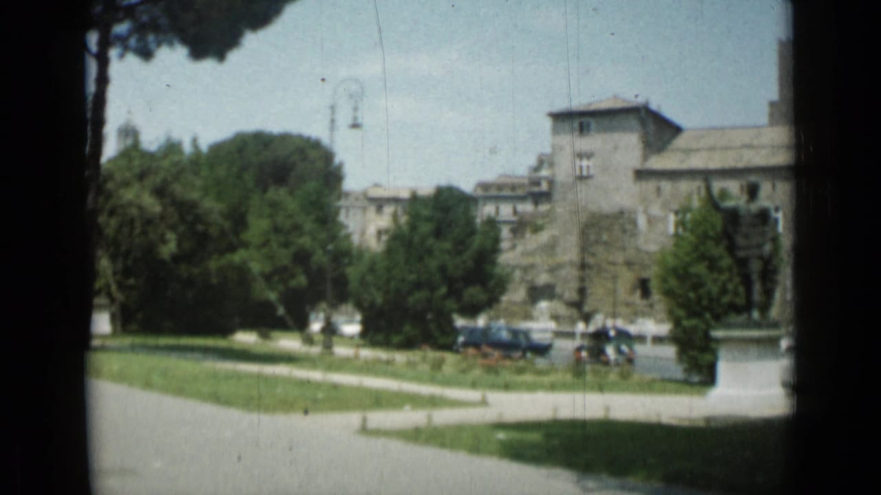 Landscaped green with trees, buildings, parked cars, and a statue at right.