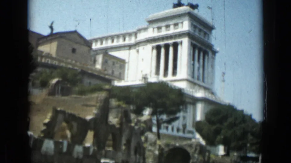 Rome 1962 home-movie frame showing the Altare della Patria behind umbrella pines and foreground ruins.