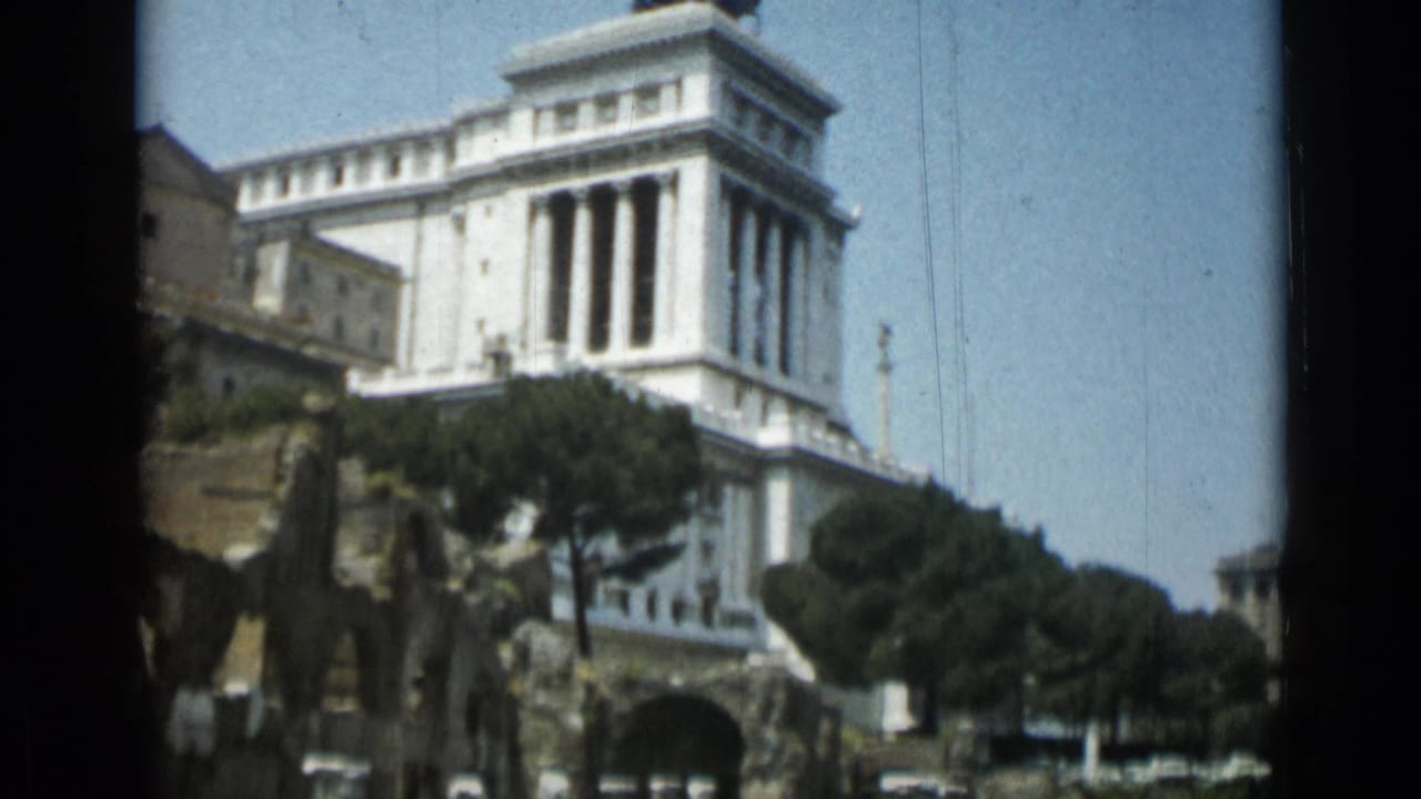 White marble monument with columns seen above trees and a roadway.