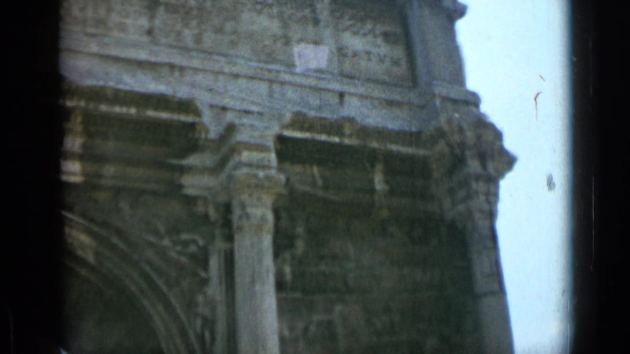 1962 8mm Rome frame showing the Arch of Constantine's inscription band, weathered column, carved stonework, and dark vertical film edges.