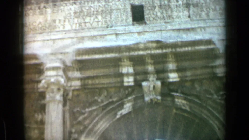 1962 8mm Rome footage frames the Arch of Constantine's inscription band, decorative relief areas, stone column, and shadowed curved opening.