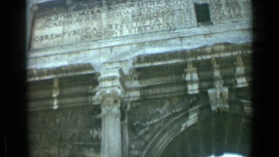 1962 Rome home-movie frame showing a close, soft-focus view of Latin inscription, relief carving, and columns on a Roman monument.