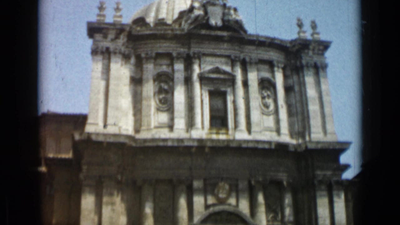1962 Rome home-movie frame showing the upper facade of a classical church with columns, niches, and part of a dome.