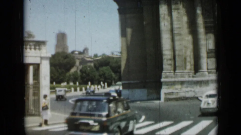 Rome street corner in 1962 with a dark car, zebra crossing, massive stone column, trees, pedestrians, and a distant dome-like structure.