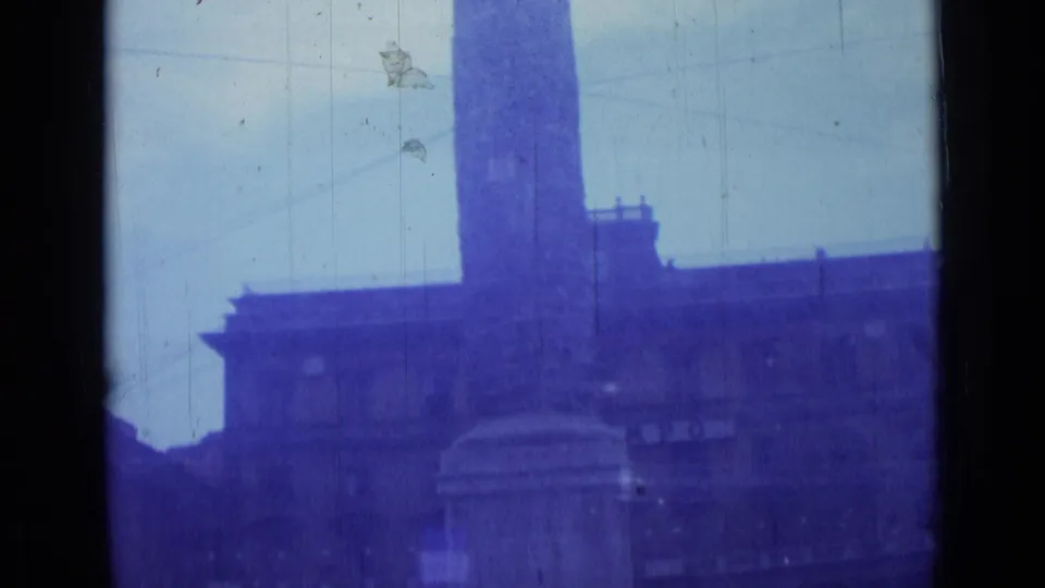 1962 Rome 8mm frame showing a tall monument with a broad pedestal before a large urban facade and pale sky.