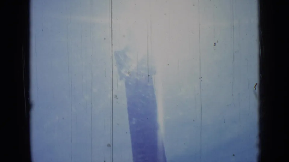 Final 1962 Rome frame with the obelisk partially veiled by sun glare, pale sky, and vertical scratches across the 8mm scan.