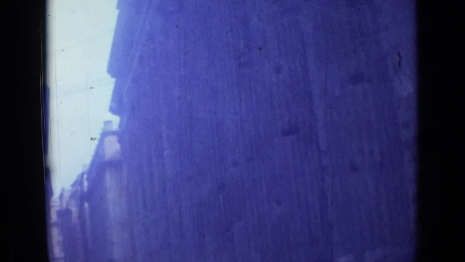 Moving-car view in Rome, 1962, with a tall wall or building face dominating the blue-shifted 8mm frame.