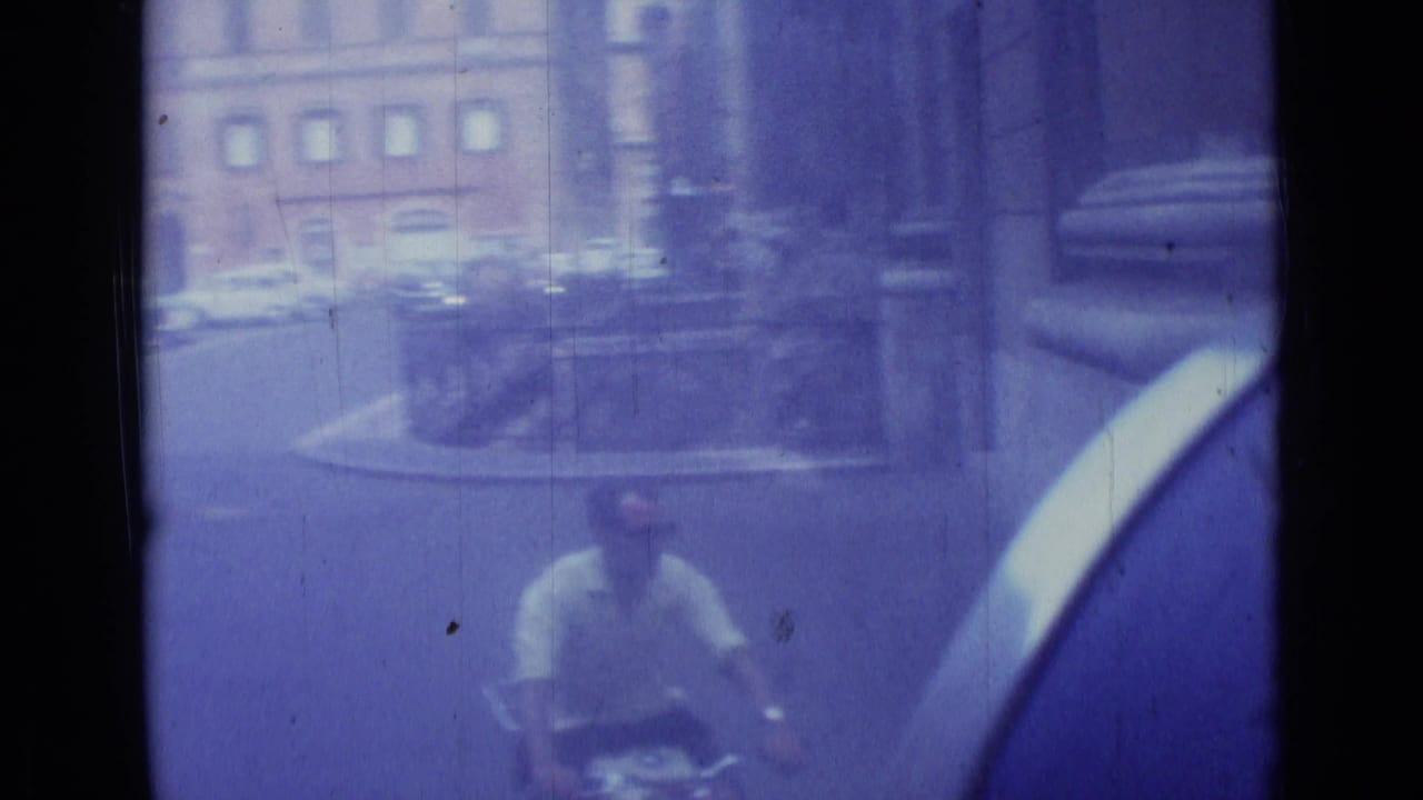 A bicyclist rides near parked cars and masonry buildings on a city street.