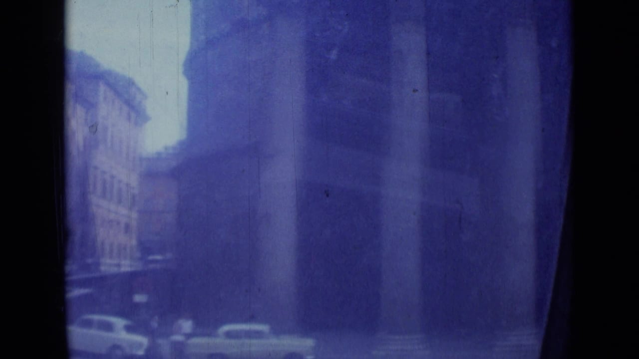 Tall buildings and parked cars appear beyond a dark vertical foreground strip.