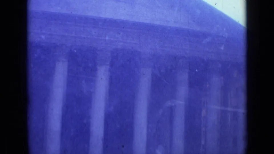 The camera holds on a columned Rome building facade, with dark gate edges, blue color shift, and soft 8mm home-movie texture.