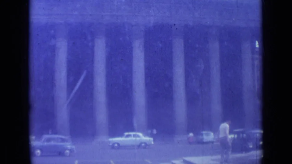 Rome street scene with tall columns in the background, several 1960s cars, and pedestrians near the curb.