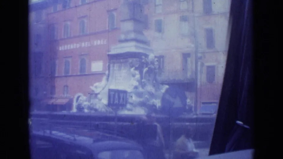 Rome city square view with a sculptural stone monument, ALBERGO DEL SOLE signage, cars, and people near the street.