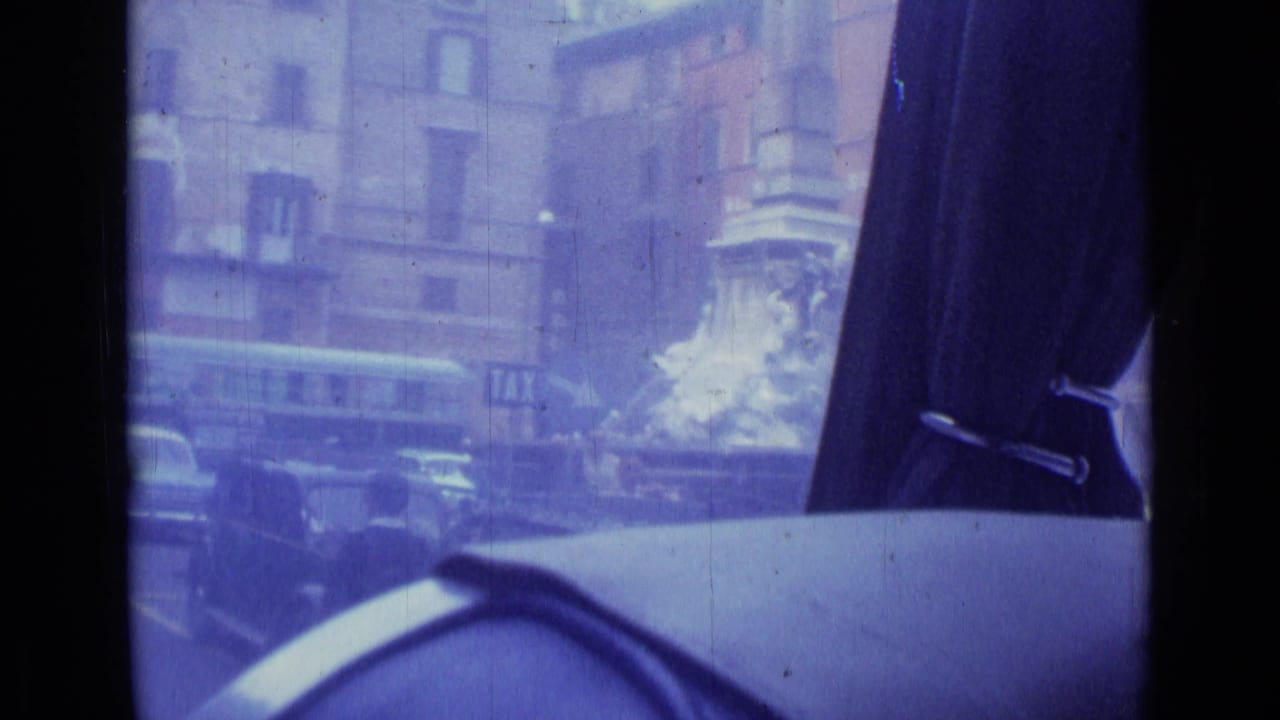 1962 Rome street view filmed from inside a vehicle, with older cars outside and a dark curtain partly blocking the frame.