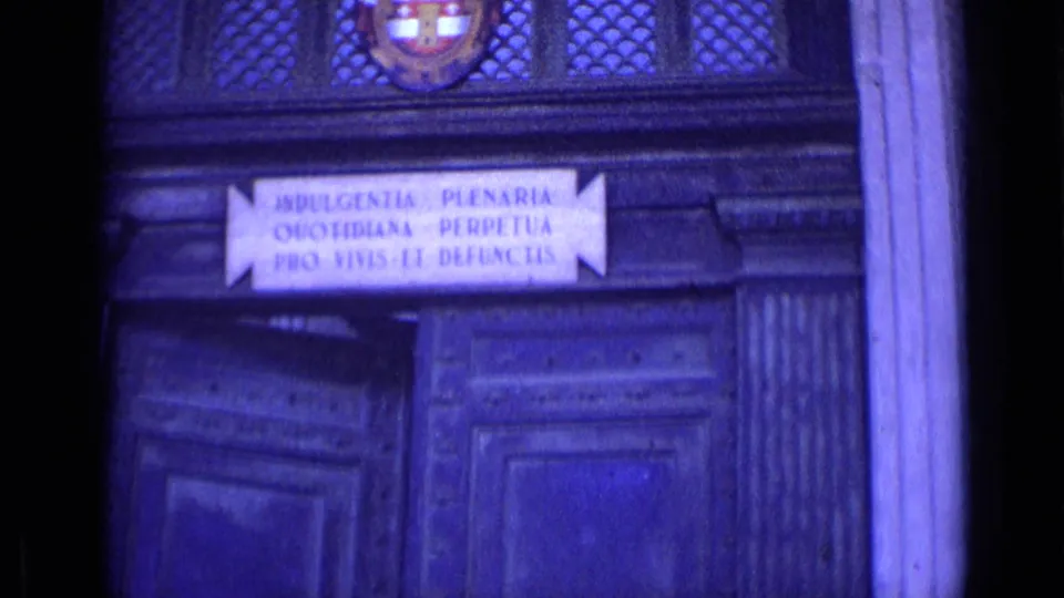 Historic doorway in Rome with carved wood panels, a Latin inscription plaque, and a coat of arms above the entrance.