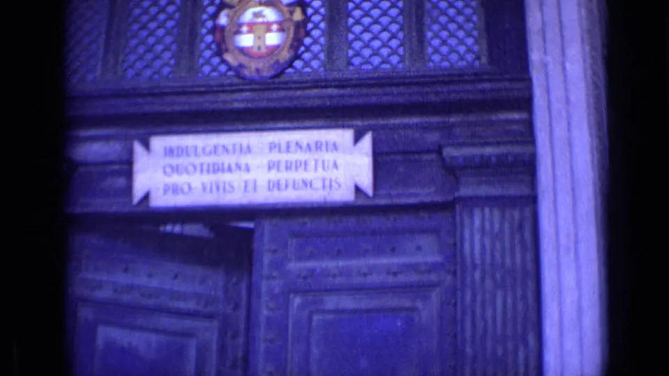 Blue-tinted 8mm frame of a Roman doorway showing a Latin sign, carved wood panels, and a decorative emblem above.