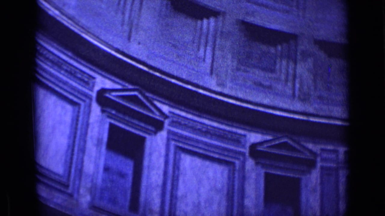 1962 Rome 8mm frame showing a curved ornate interior wall, classical panels, and shadowed openings below a high circular ceiling.