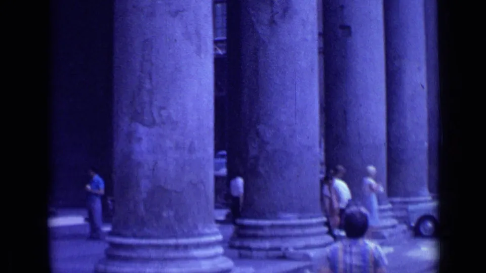 1962 Rome footage showing a row of large classical columns with pedestrians walking through sun and shadow along the street.