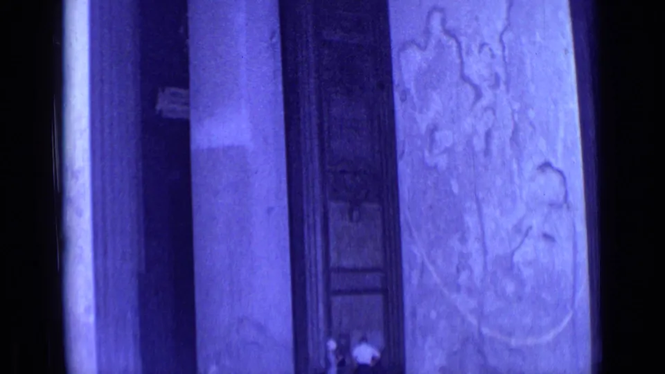 Blue-shifted 1962 Rome frame with monumental columns, a tall doorway or window, and small visitors at the base for scale.