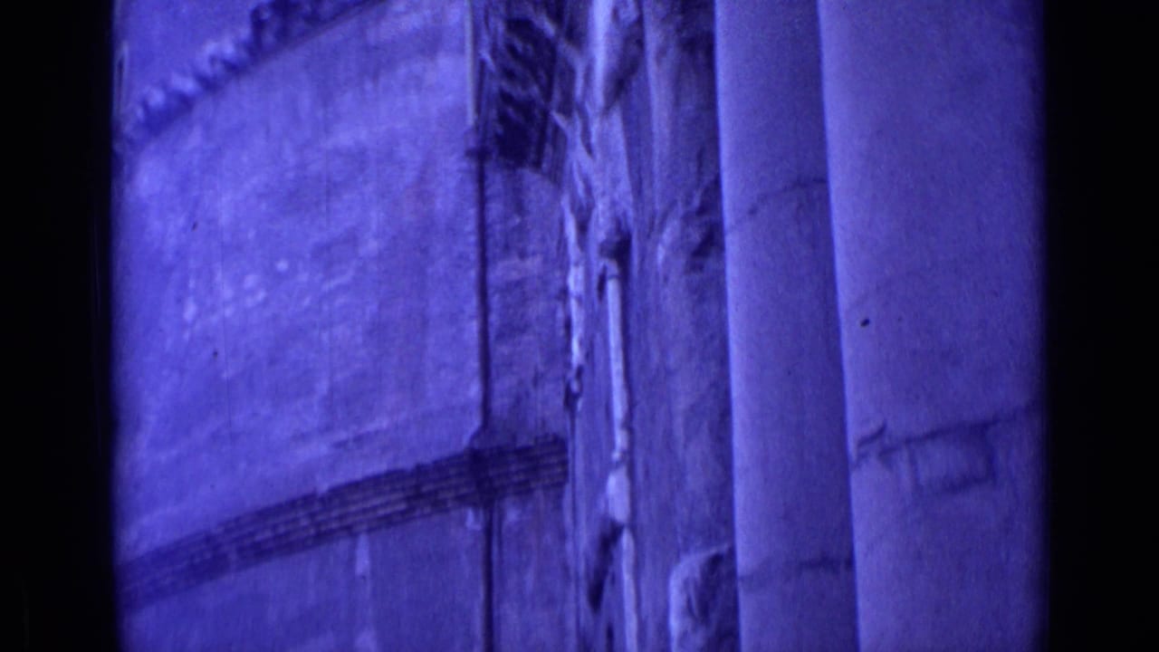 1962 Rome home-movie frame showing a purple-tinted architectural facade with vertical columns and textured wall surfaces.
