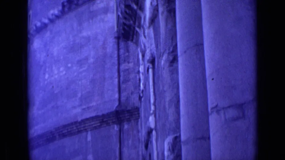 1962 Rome home-movie frame showing a purple-tinted architectural facade with vertical columns and textured wall surfaces.