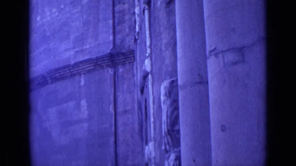 Purple-tinted 8mm frame from Rome showing a close architectural surface, vertical columns, and a dark central film edge.