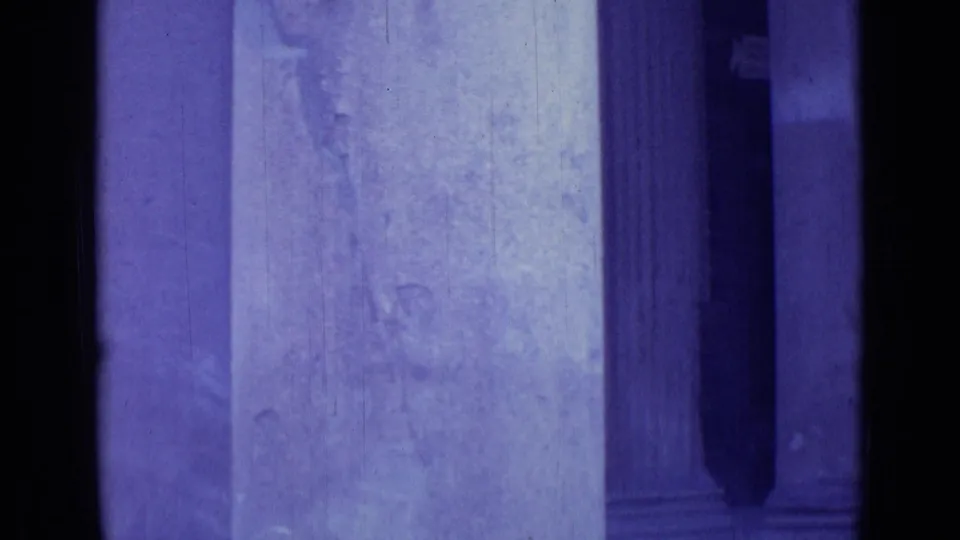 1962 Rome 8mm frame showing a bright stone wall, doorway edge, and deep shadowed recess under strong purple-tinted exposure.