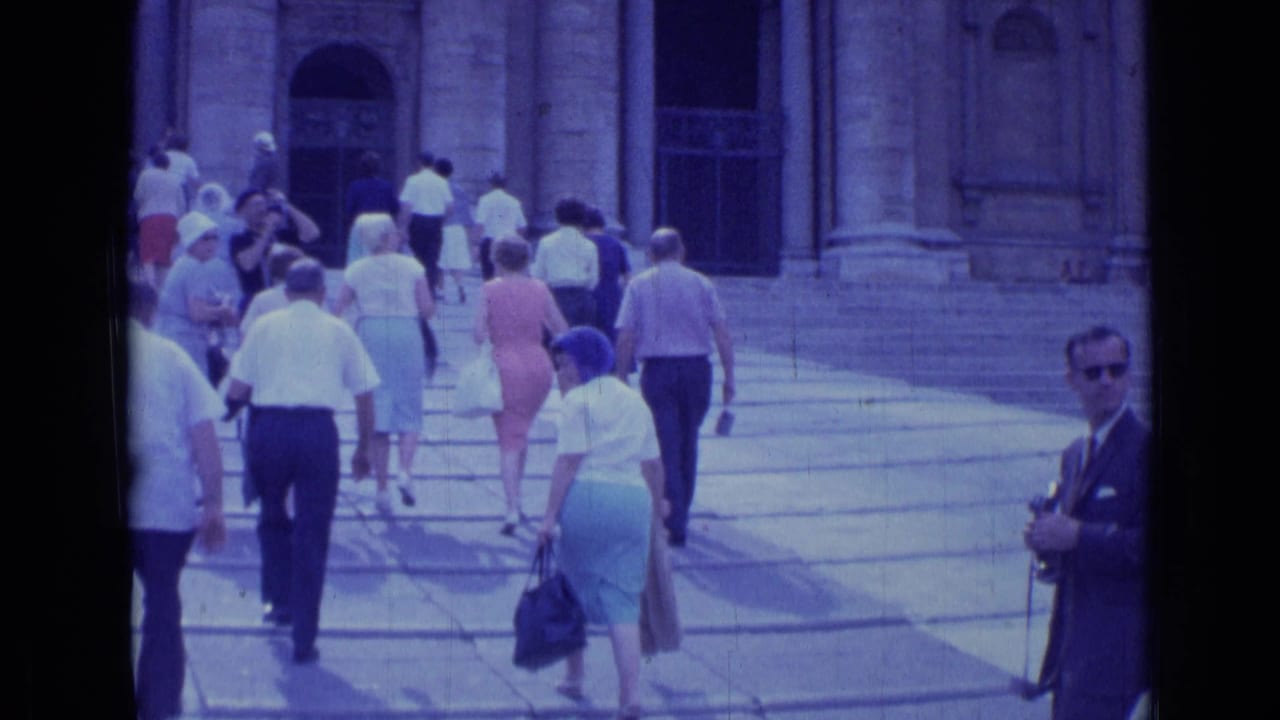 1962 Rome home-movie frame showing tourists in summer clothing ascending steps toward a grand classical facade.