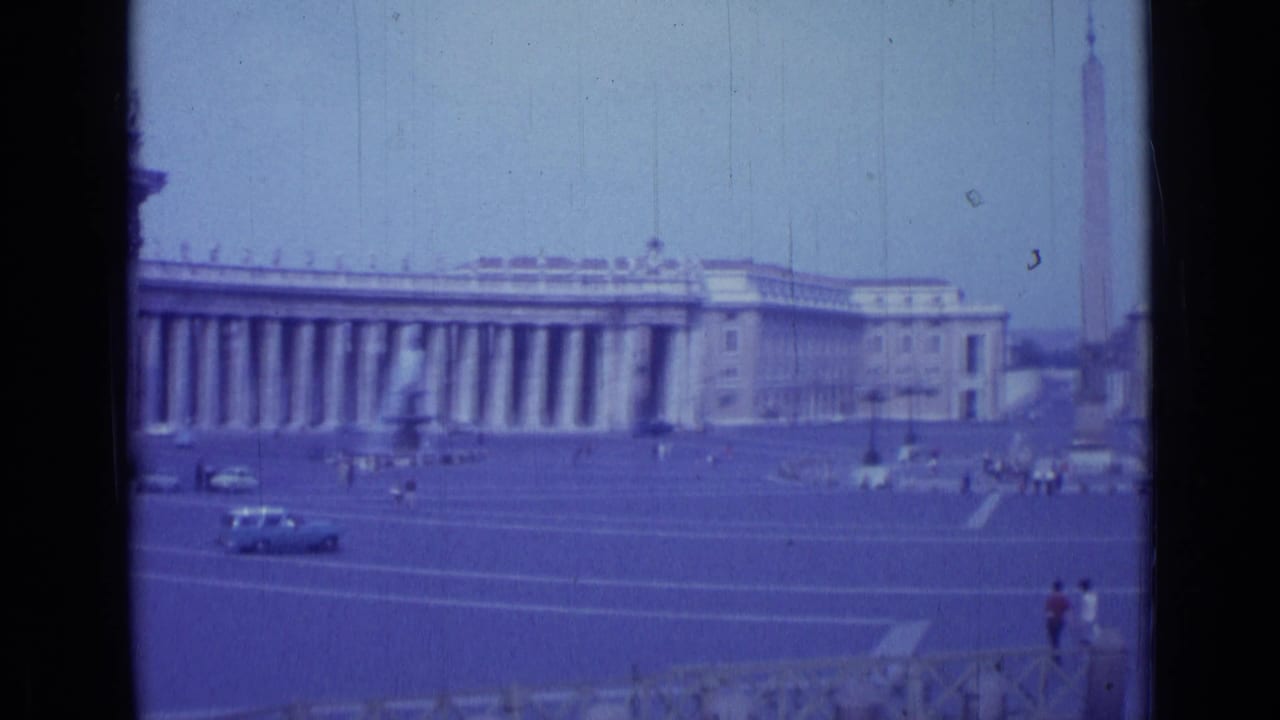 Wide view of St. Peter's Square with colonnades, obelisk, cars, and visitors.