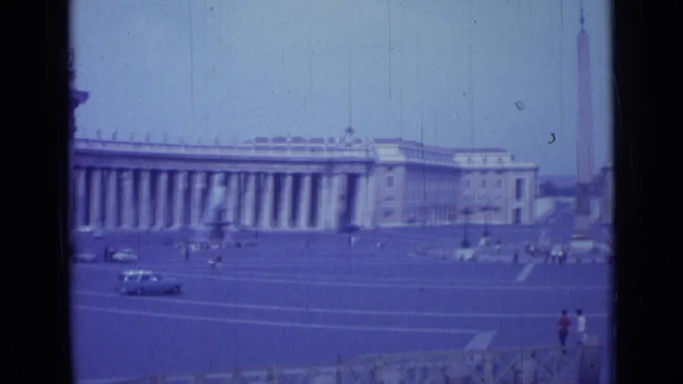 1962 Rome travel frame showing St. Peter's Square, the central obelisk, long colonnades, small groups of visitors, and cars in the plaza.