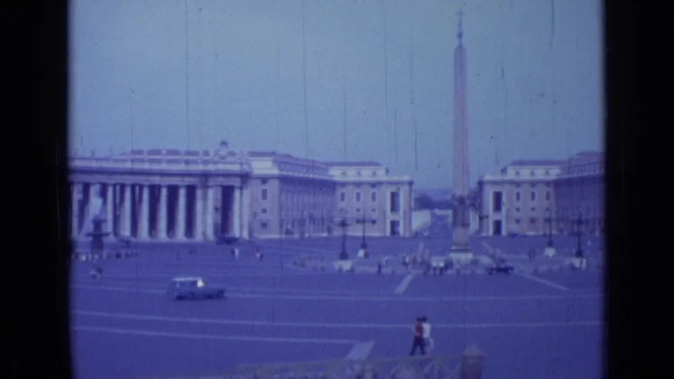 Home-movie frame from 1962 showing St. Peter's Square in Rome with the obelisk centered between colonnades and cars moving through the plaza.