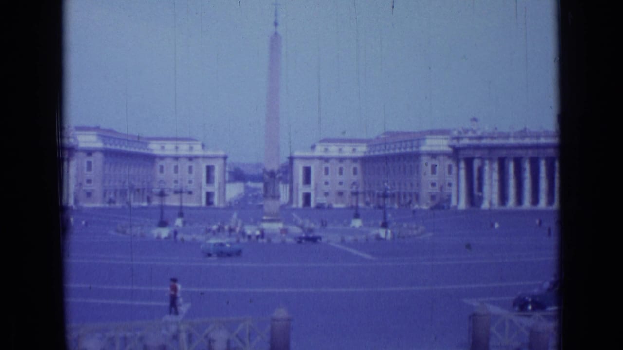 1962 8mm view across St. Peter's Square in Vatican City, showing the central obelisk, colonnades, period cars, and small pedestrians.
