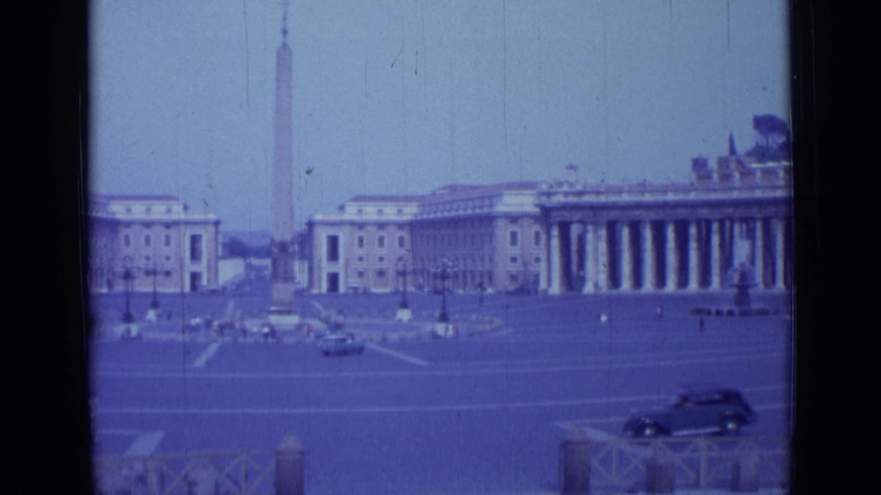 Wide Vatican square view with obelisk, colonnades, dark car, and pedestrians in the distance.