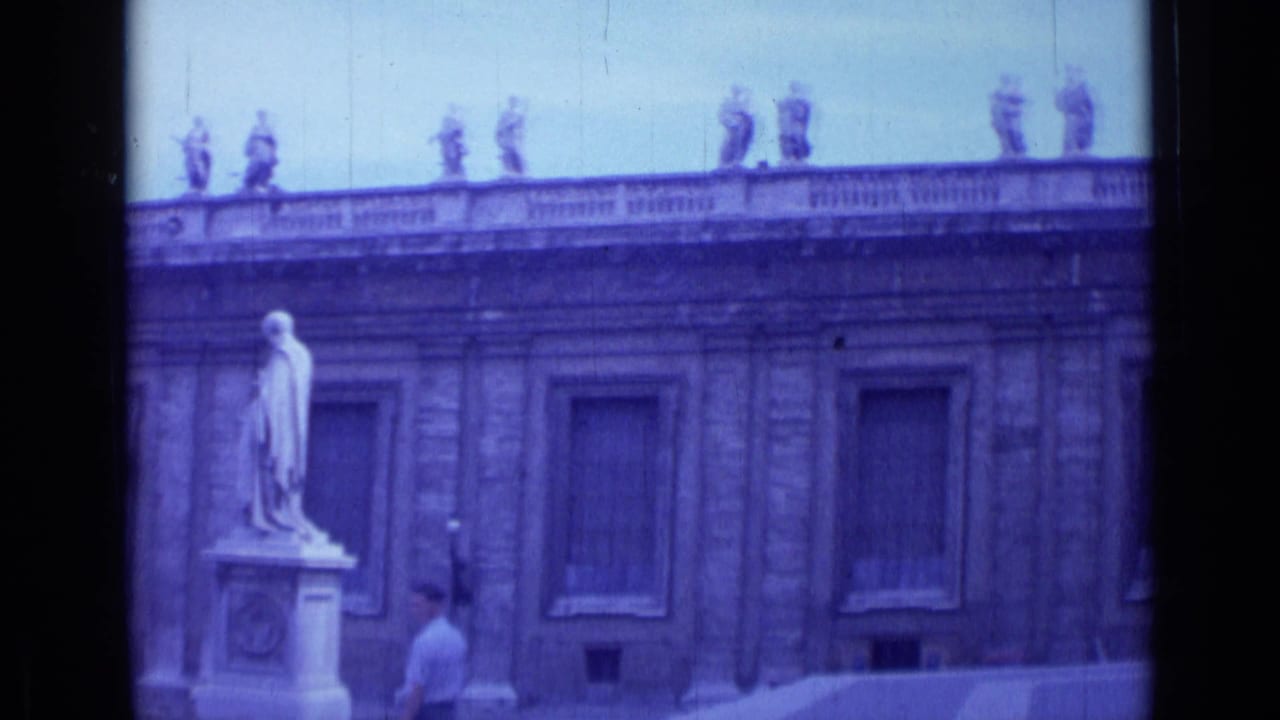 Classical building facade with a foreground statue and a tourist walking near shuttered windows.