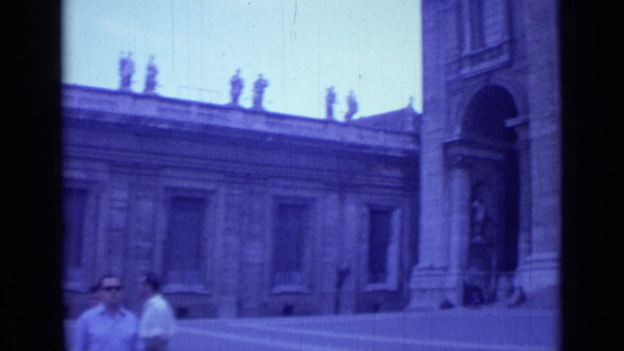 Adult visitors stand near a church courtyard facade with an arched doorway at the right edge.