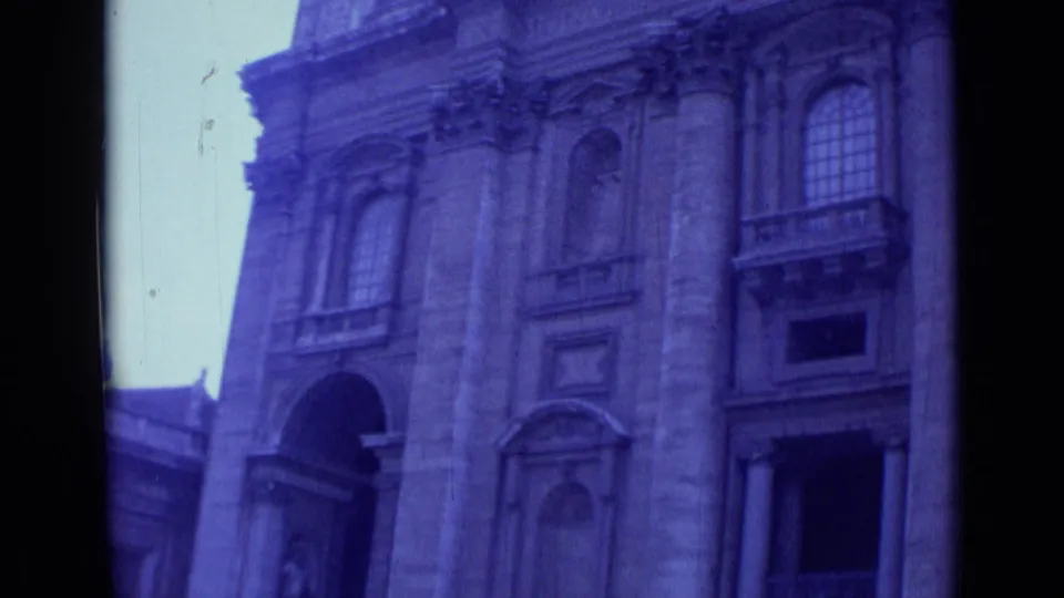 Rome 1962 frame emphasizing a monumental church facade with stone columns, arched portals, tall windows, and blue-tinted 8mm texture.