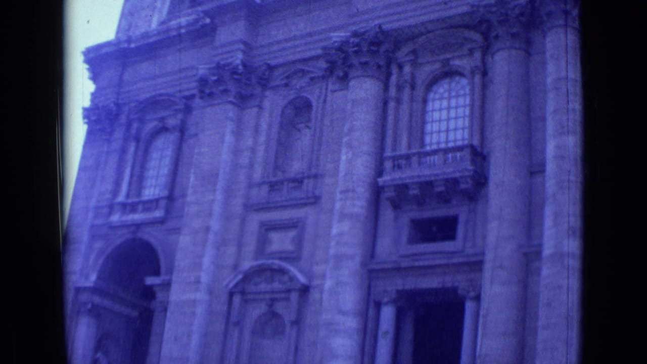 Upward view of a stone facade with tall columns, arched windows, and dark film borders.