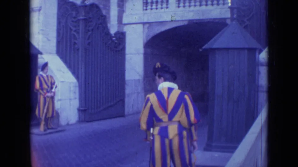 1962 Rome frame showing Swiss Guards in striped ceremonial uniforms near an ornate iron gate and sentry box.