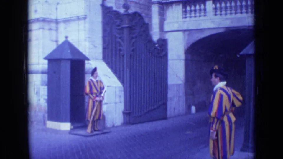 1962 Rome home-movie frame showing Swiss Guard-style ceremonial guards by an ornate gate and small sentry box.