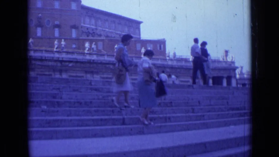 1962 Rome travel-film frame showing women with handbags and other visitors ascending wide stone steps near a large building.